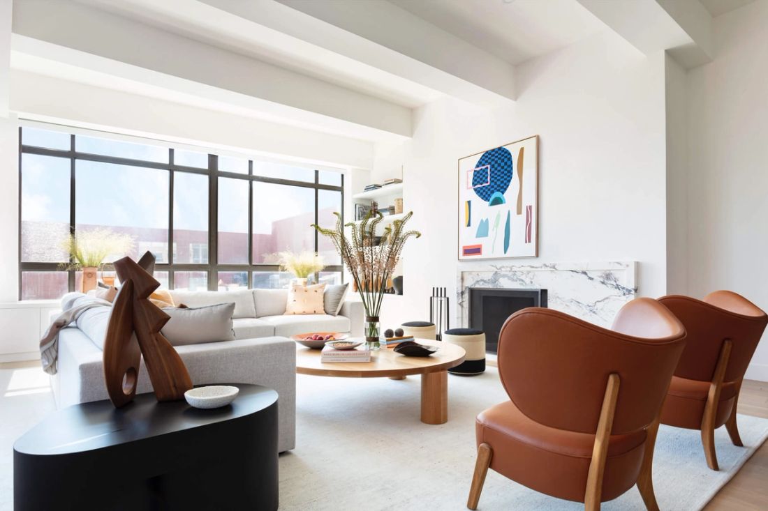 Living room with white walls, and white painted rafters with marble fireplace, comfy whisky-colored leather chairs opposite soft-gray L-shaped sofa and custom coffee table