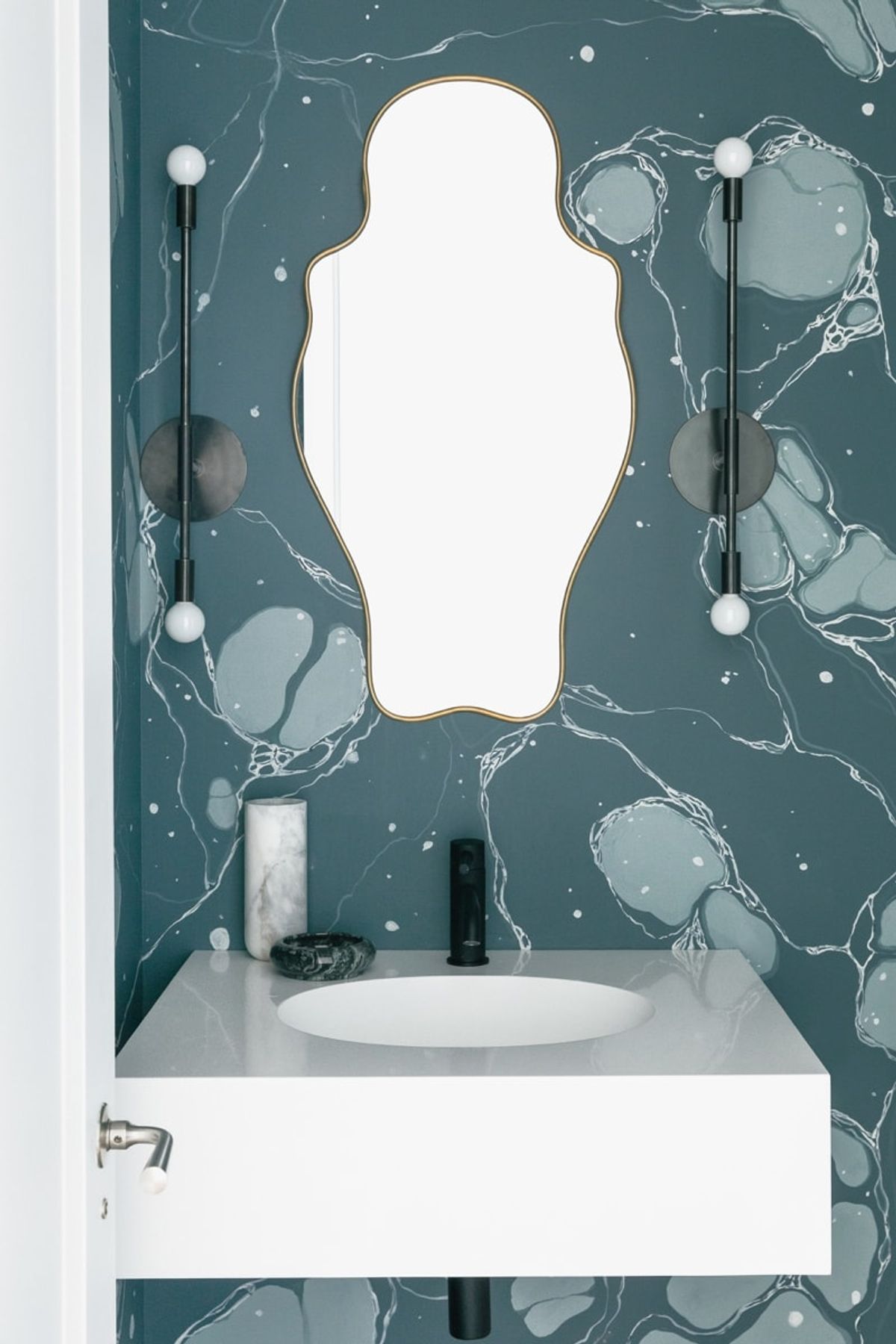 Powder room with curvy mirror and patterned wallpaper