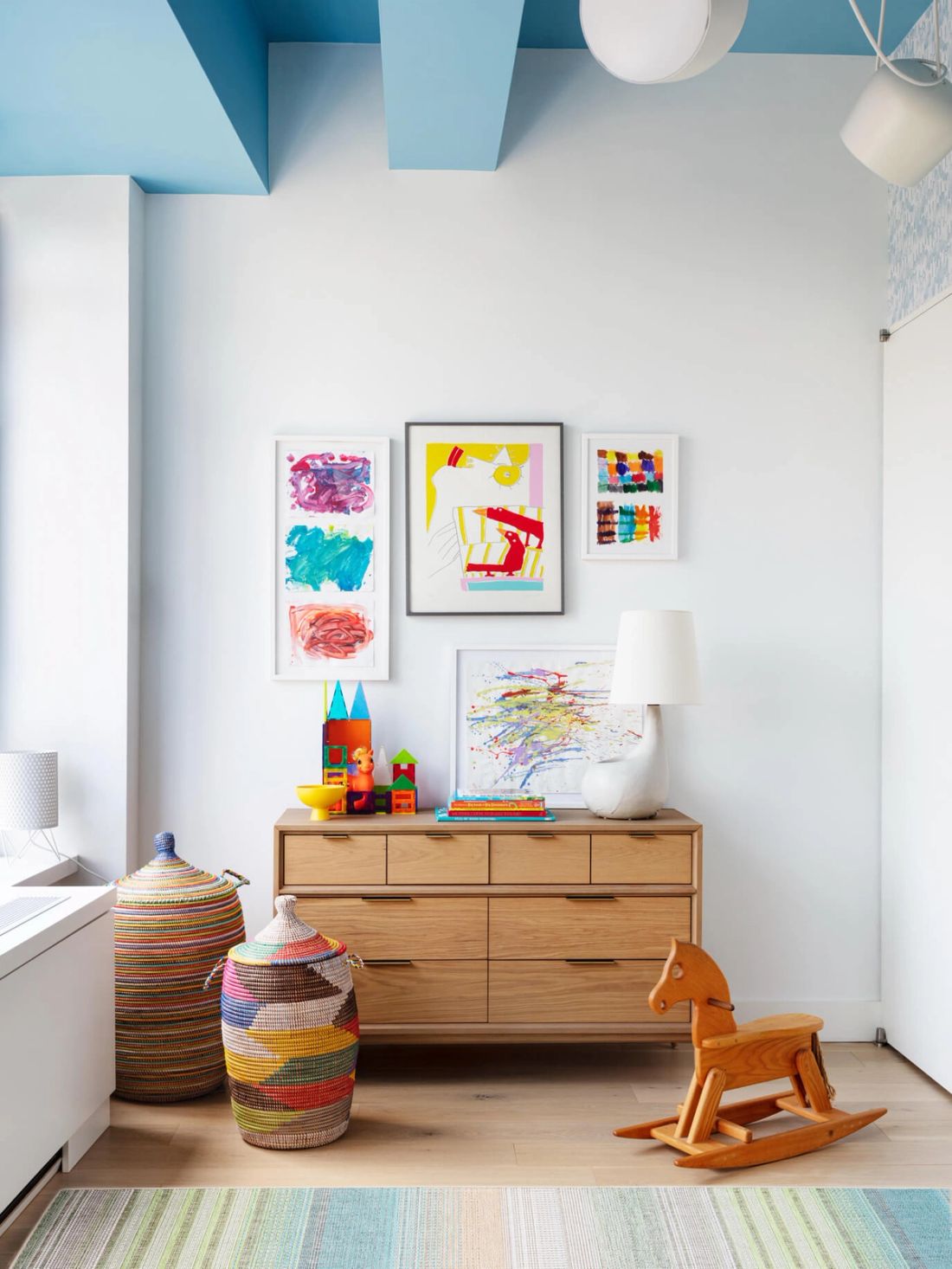 Vignette of wood dresser in child's room with colorful artwork by the resident on the wall amid toys and colorful woven baskets