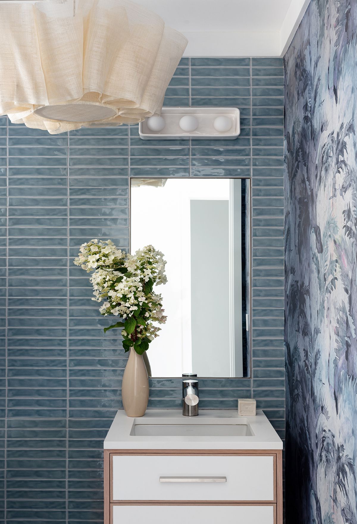 Bathroom with blue tile and complimentary wallpaper and sink with drawers beneath