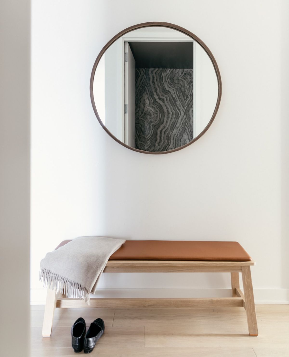 Foyer with wood bench and leather cushion under round mirror