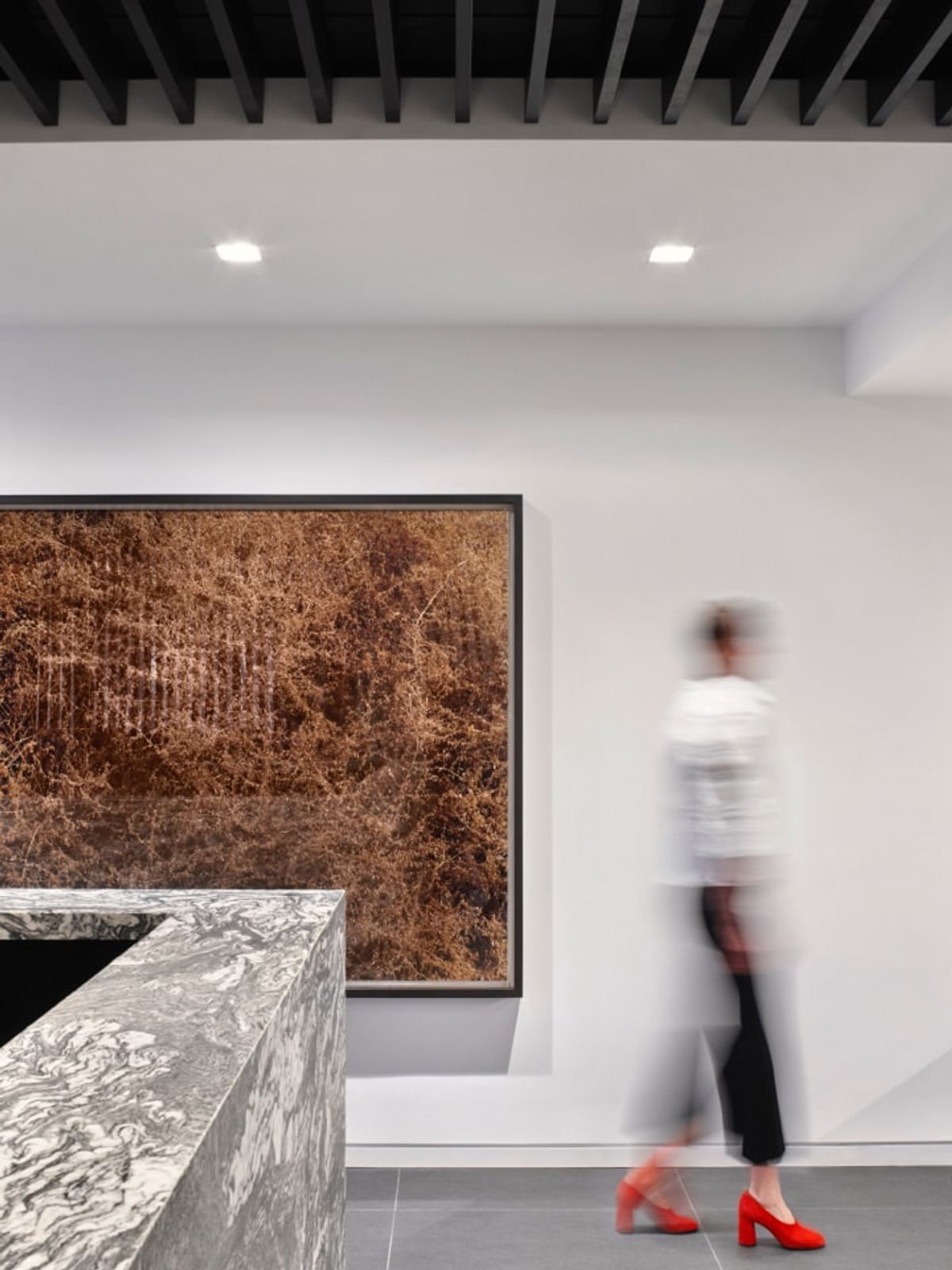 Detail of reception desk and artwork; woman in red high heels walking through the fram