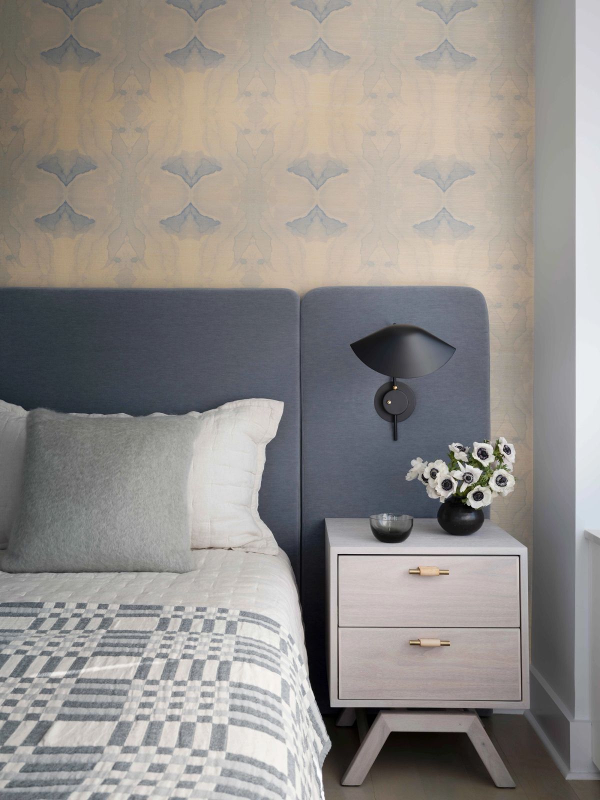 Vignette of bed with wallpaper, sconce and side table