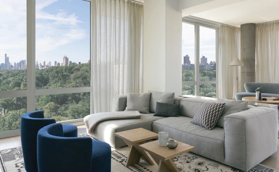 Primary seating area with gray sofa and two blue chairs opposite adjacent to wall-sized windows