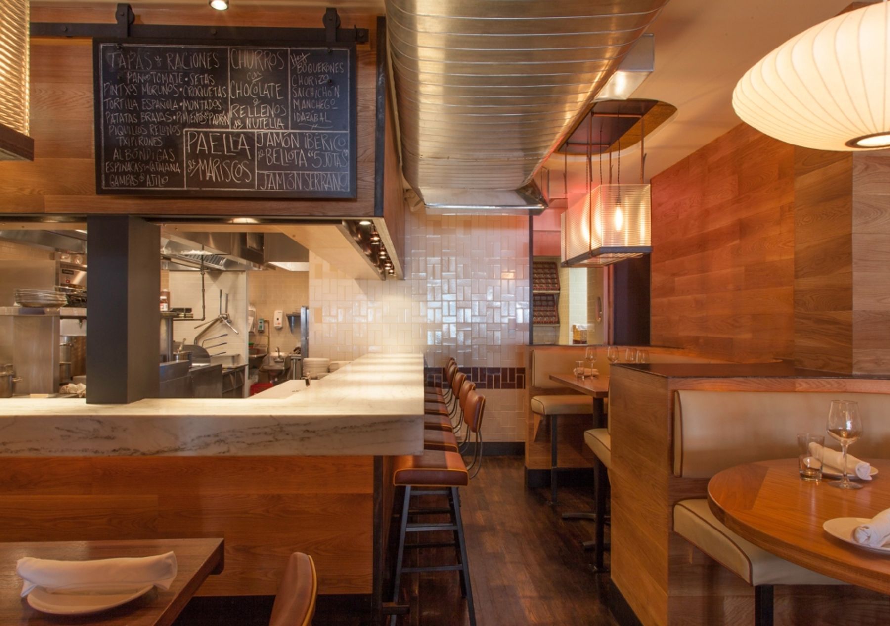 Warm honey-colored wood with marble countertop at bar that looks into the kitchen and booths and tables surrounding