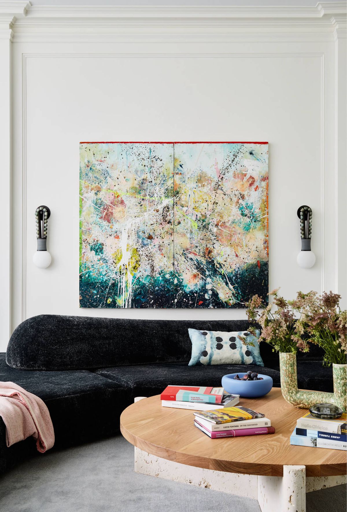 Vignette of curved sofa and low coffee table with colorful artwork and wall sconces on either side