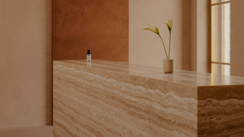 Edler Travertin-Empfangstresen mit Blume in warmem Praxisinterieur — Premium-Positionierung ohne Rabatte