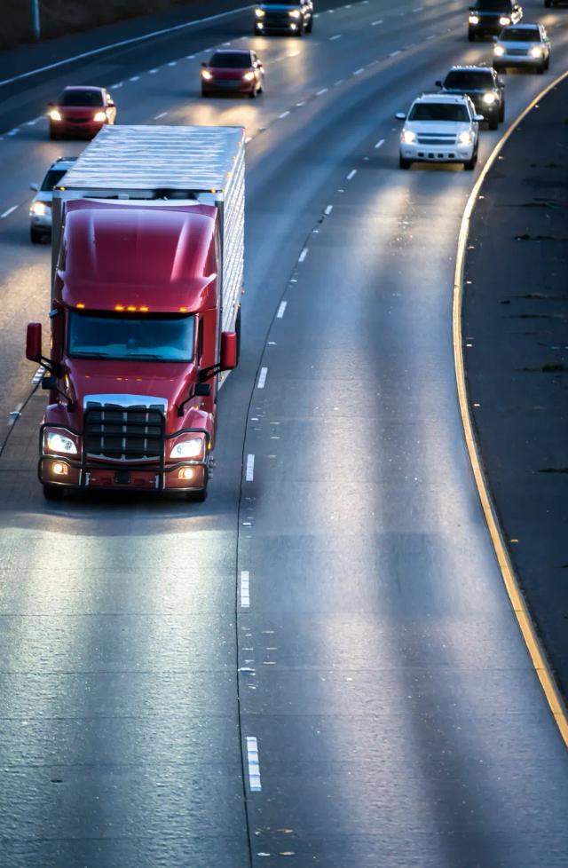 A red semi truck driving down a highway at night.