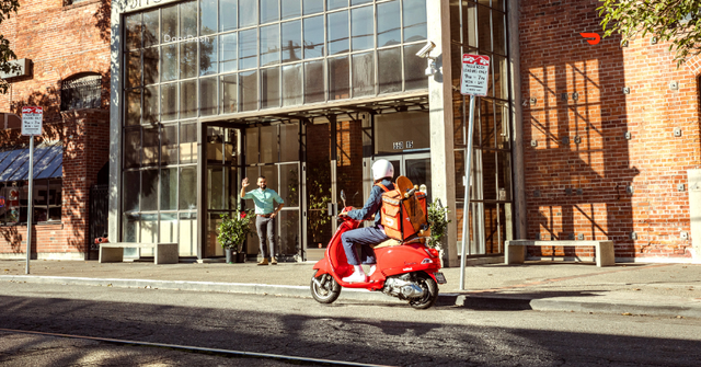 A man riding a red scooter in front of a brick building.