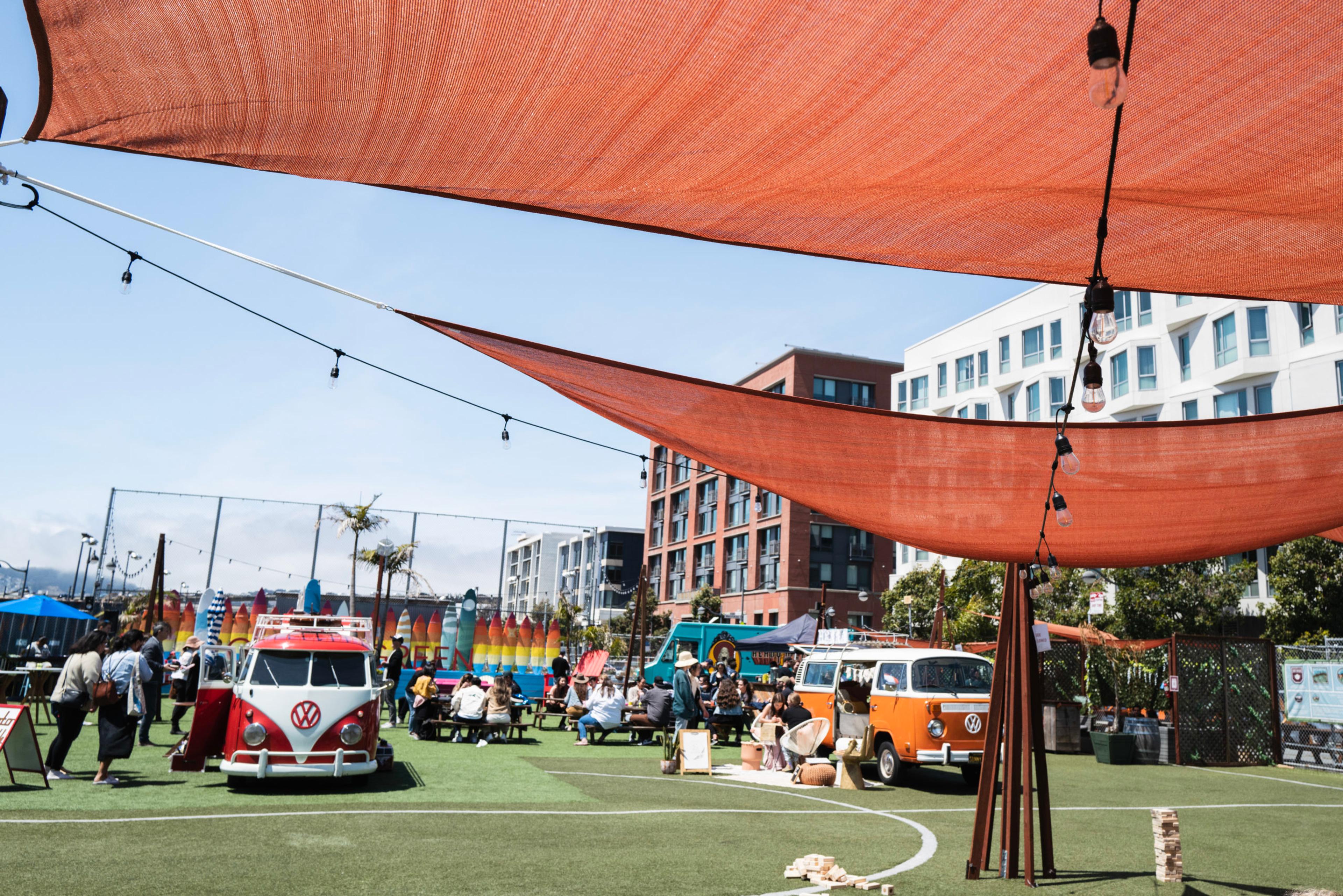A large orange umbrella is hanging over a field with a red and white truck and a van.