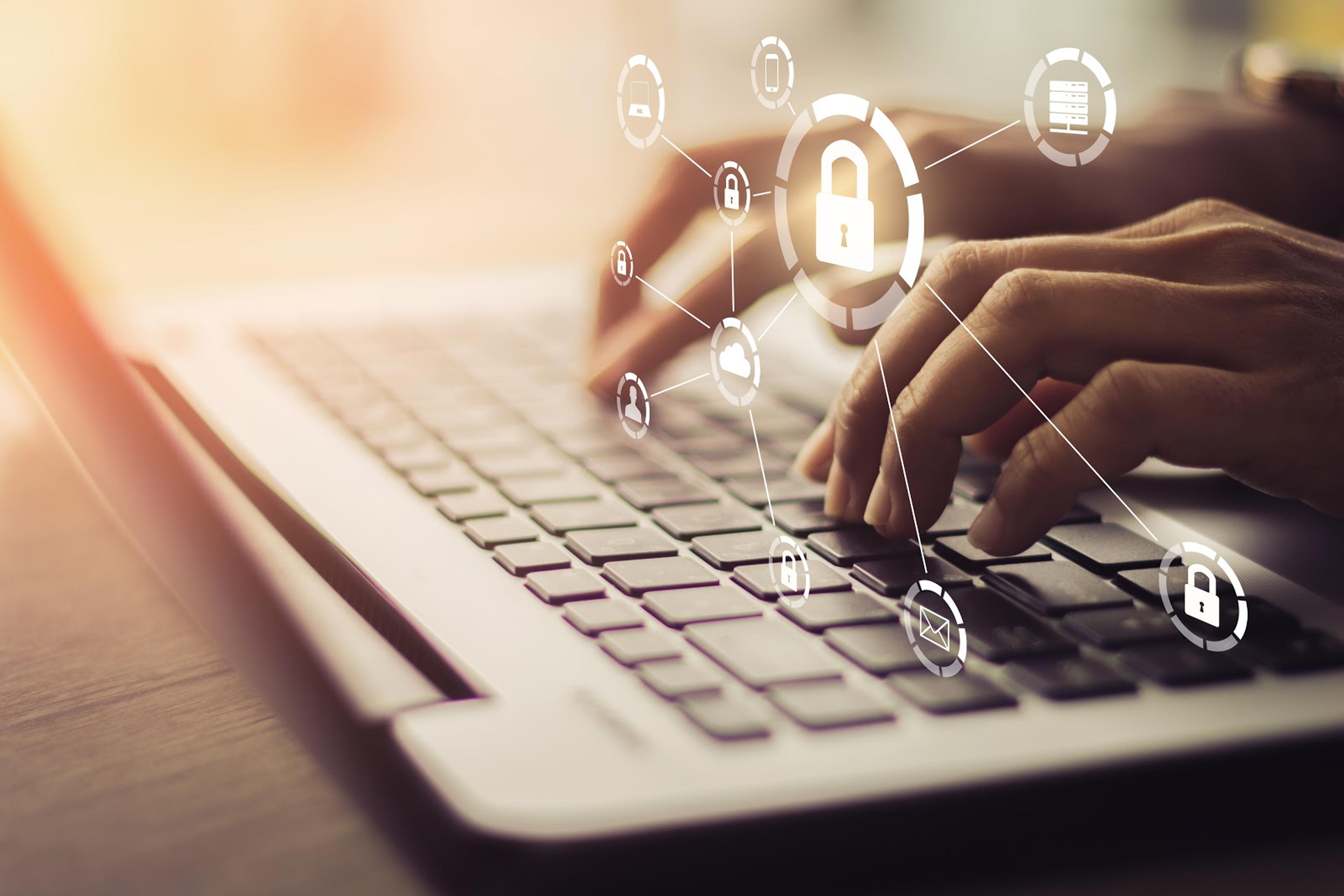 A person is typing on a laptop with a security lock on the keyboard.