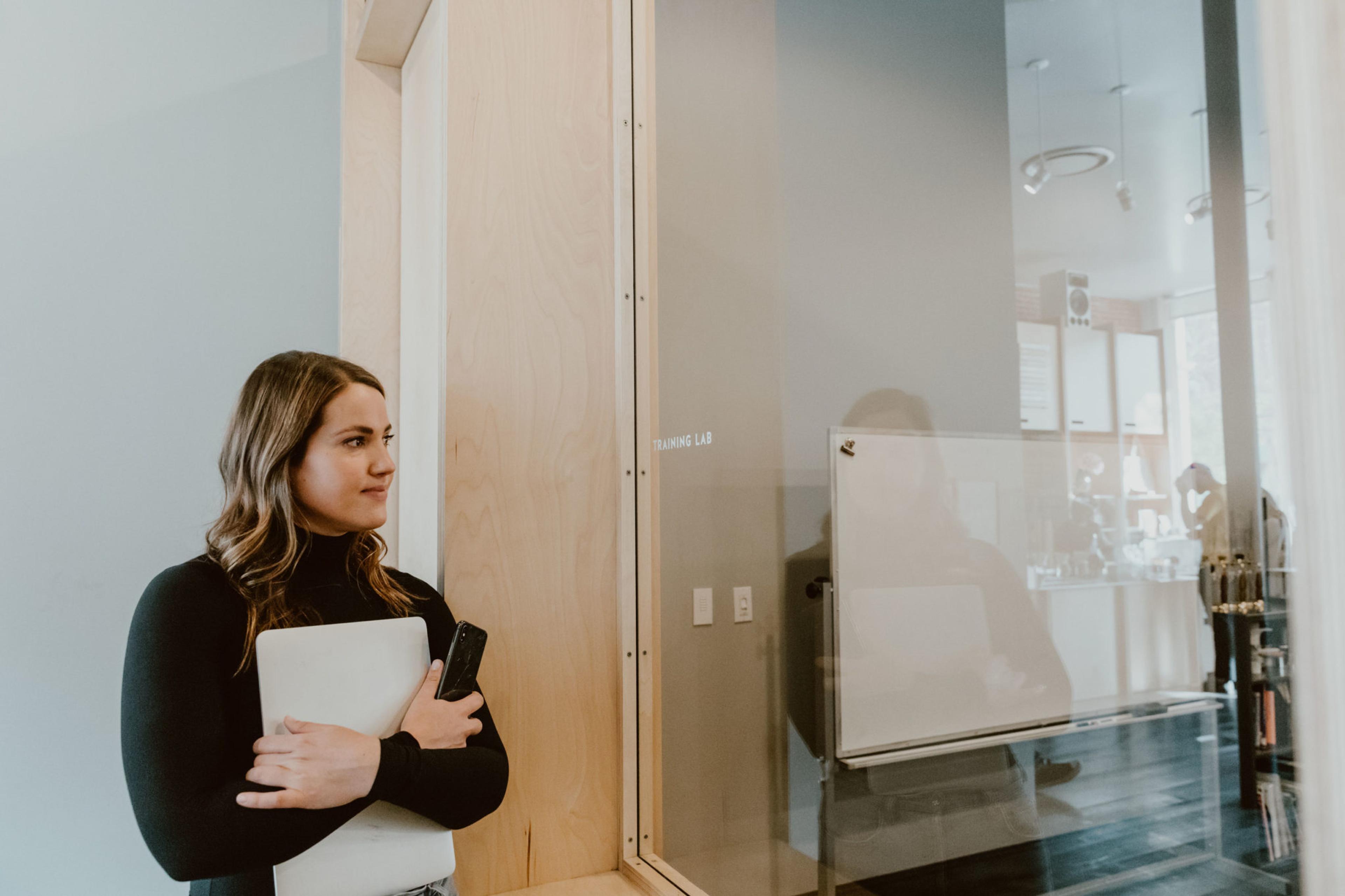 A woman with a laptop and a book bag standing in front of a glass wall.