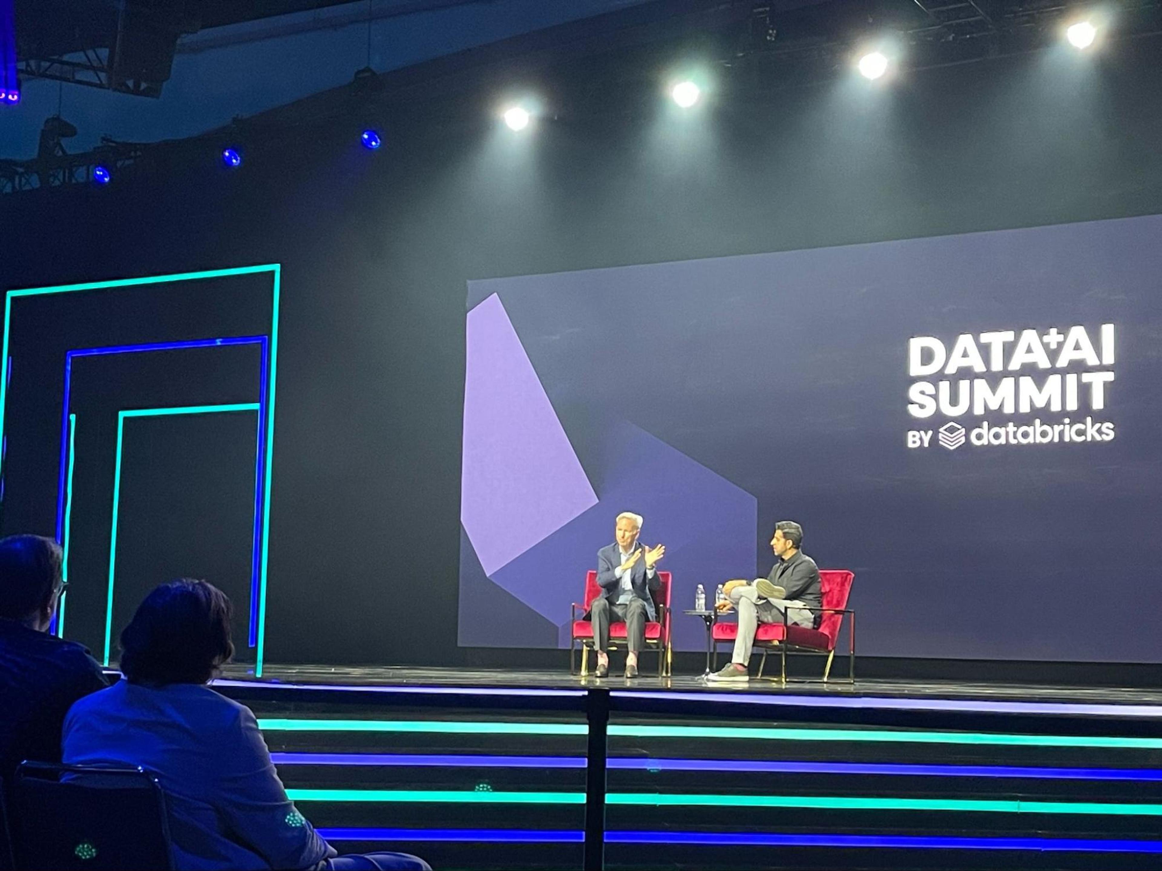 Two men are sitting on chairs on a stage at a Data Summit.