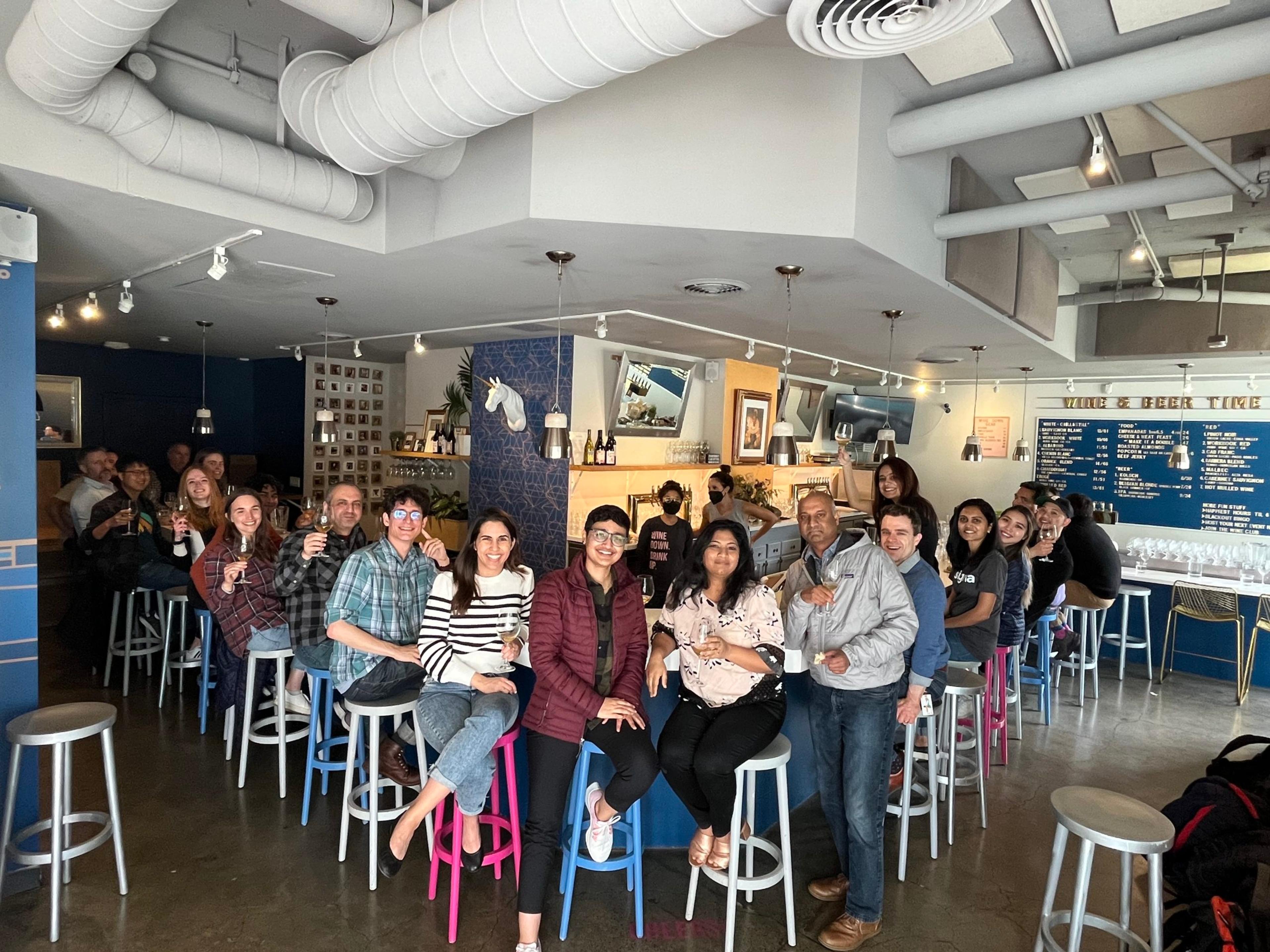 A group of people sitting at a bar with a pink and blue stool.