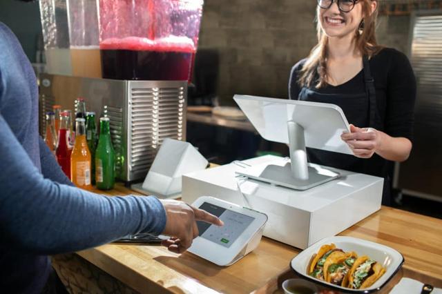 A man is using a device at a counter with a woman standing behind him.