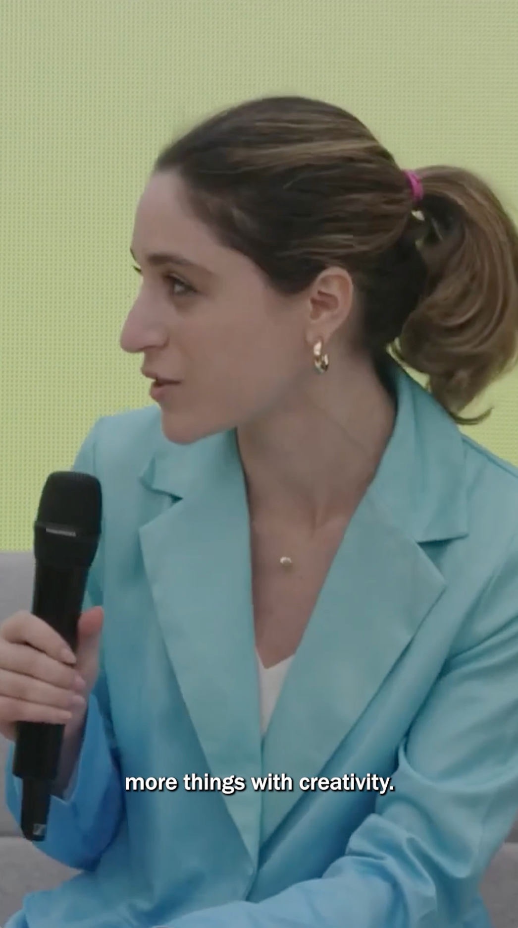 Talia Cotton sits in a light blue blazer, holding a black handheld microphone and speaking while looking to the side. Her brown hair is pulled back in a ponytail, and the on-screen caption reads, “more things with creativity.”