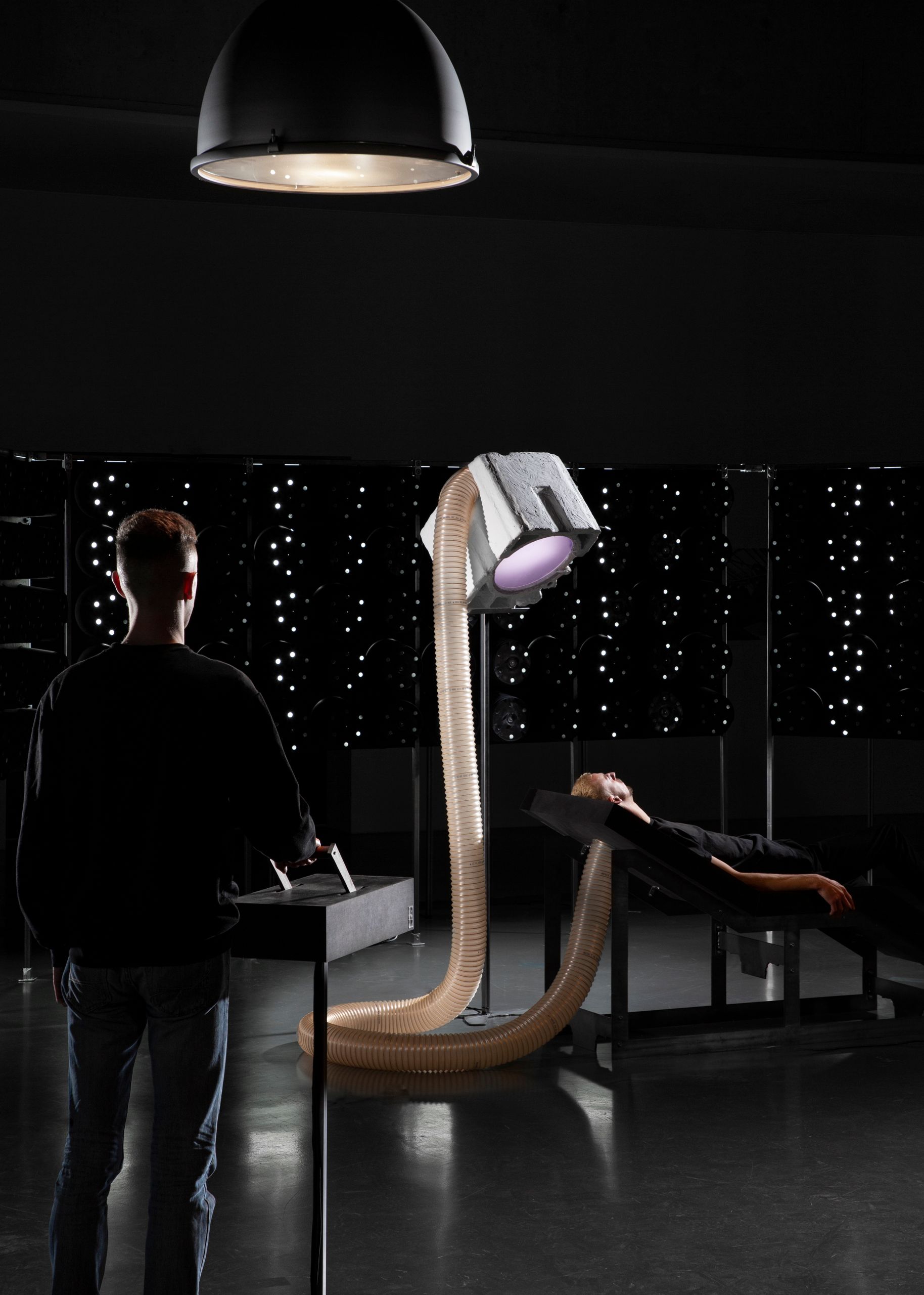Projet de diplôme master design espace et communication tommy poiré, Chaise longue dans laboratoire expérimental entourée de faisceaux lumineux et d'un projecteur de lumière relié à la table par un tube à soufflet