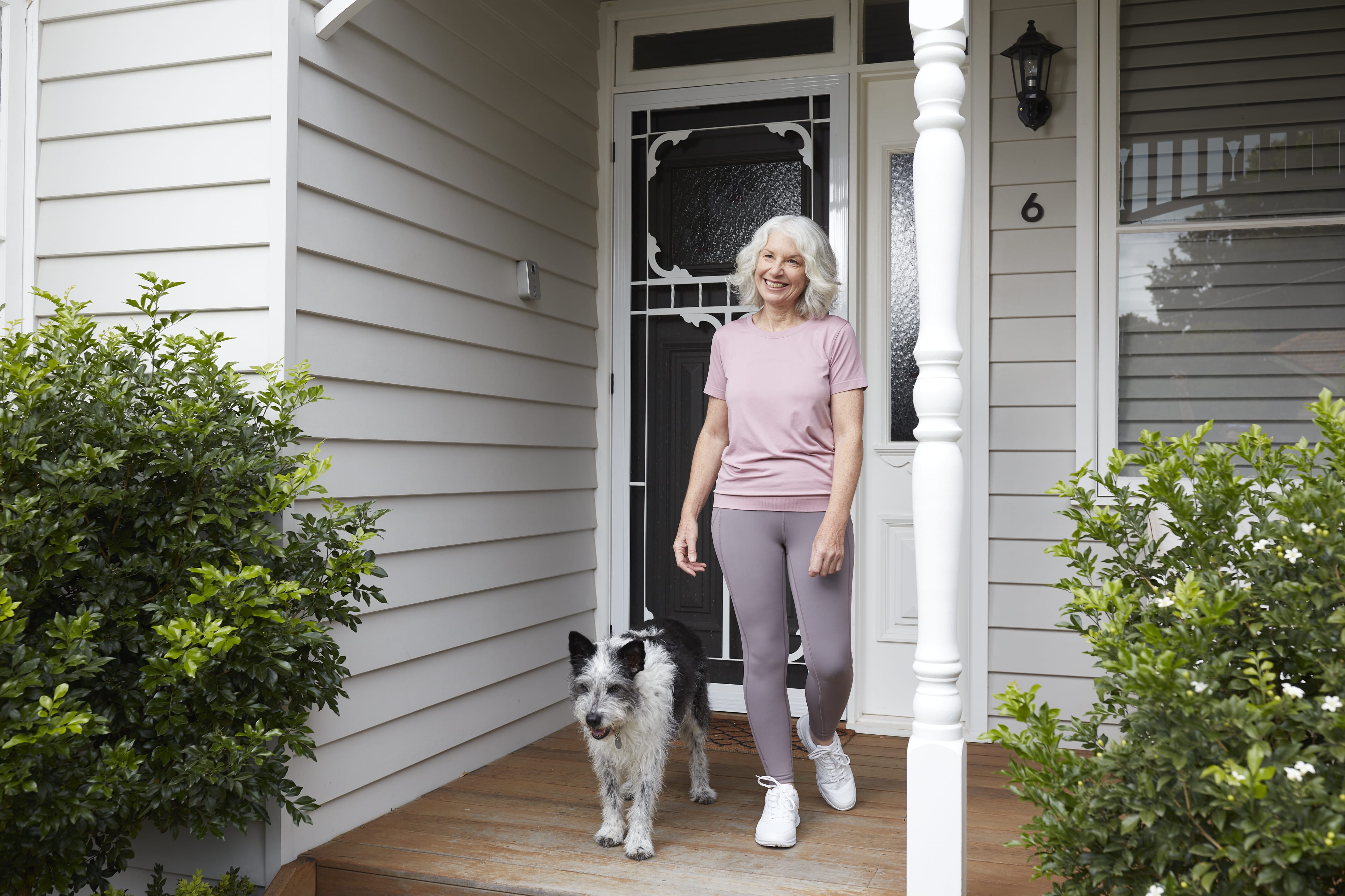A woman with her dog stands on her front veranda