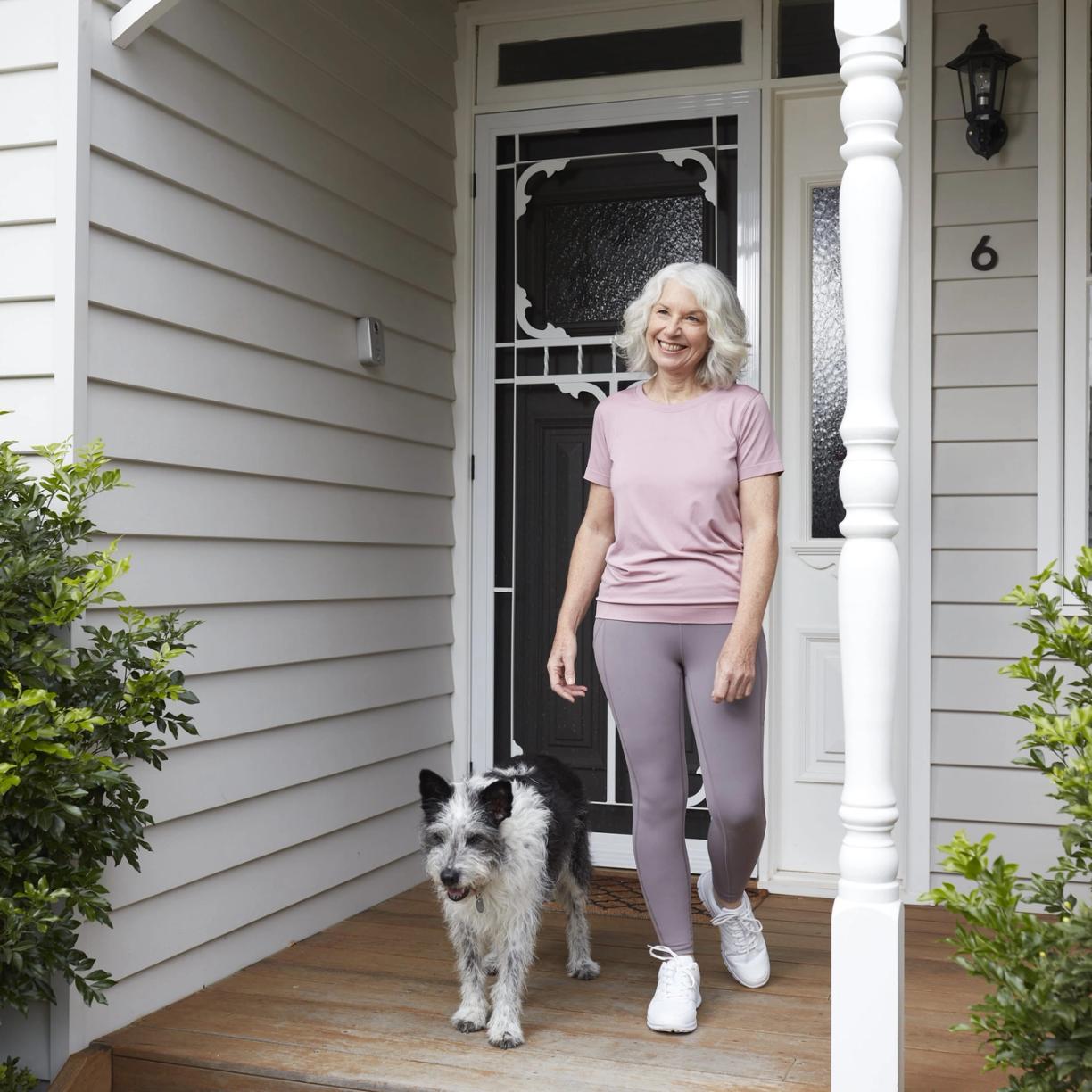 A woman with her dog stands on her front veranda