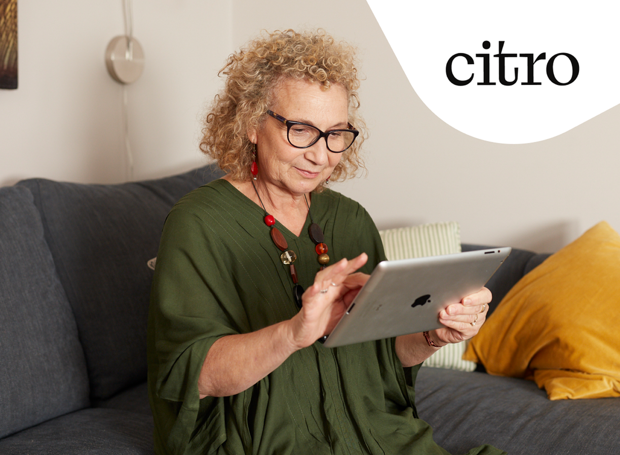 A woman seated on a sofa using a tablet to review her home finances.