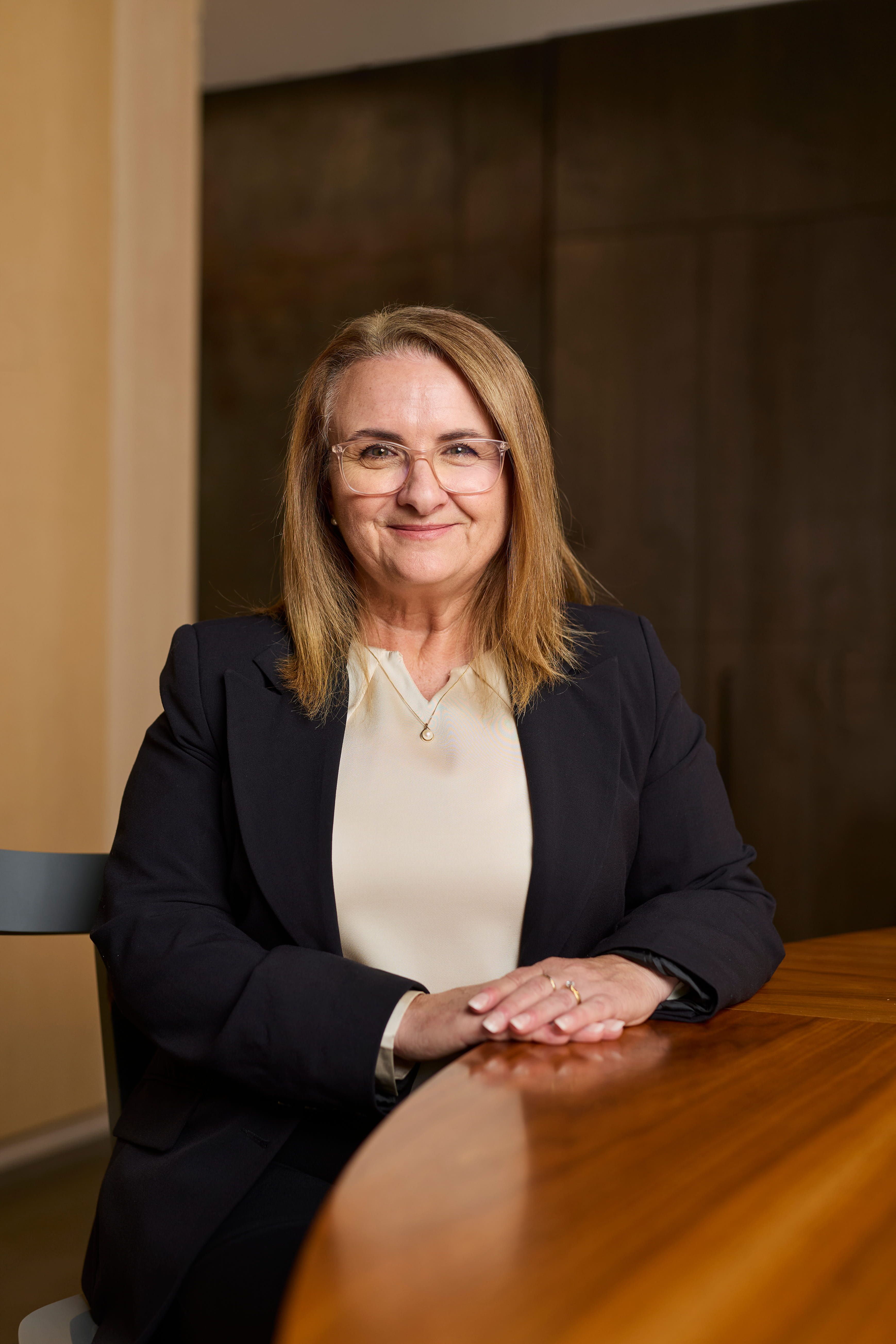 A woman in a blazer sits smiling to camera