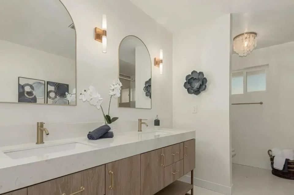 Remodeled bathroom with a double vanity, arched mirrors and gold fixtures