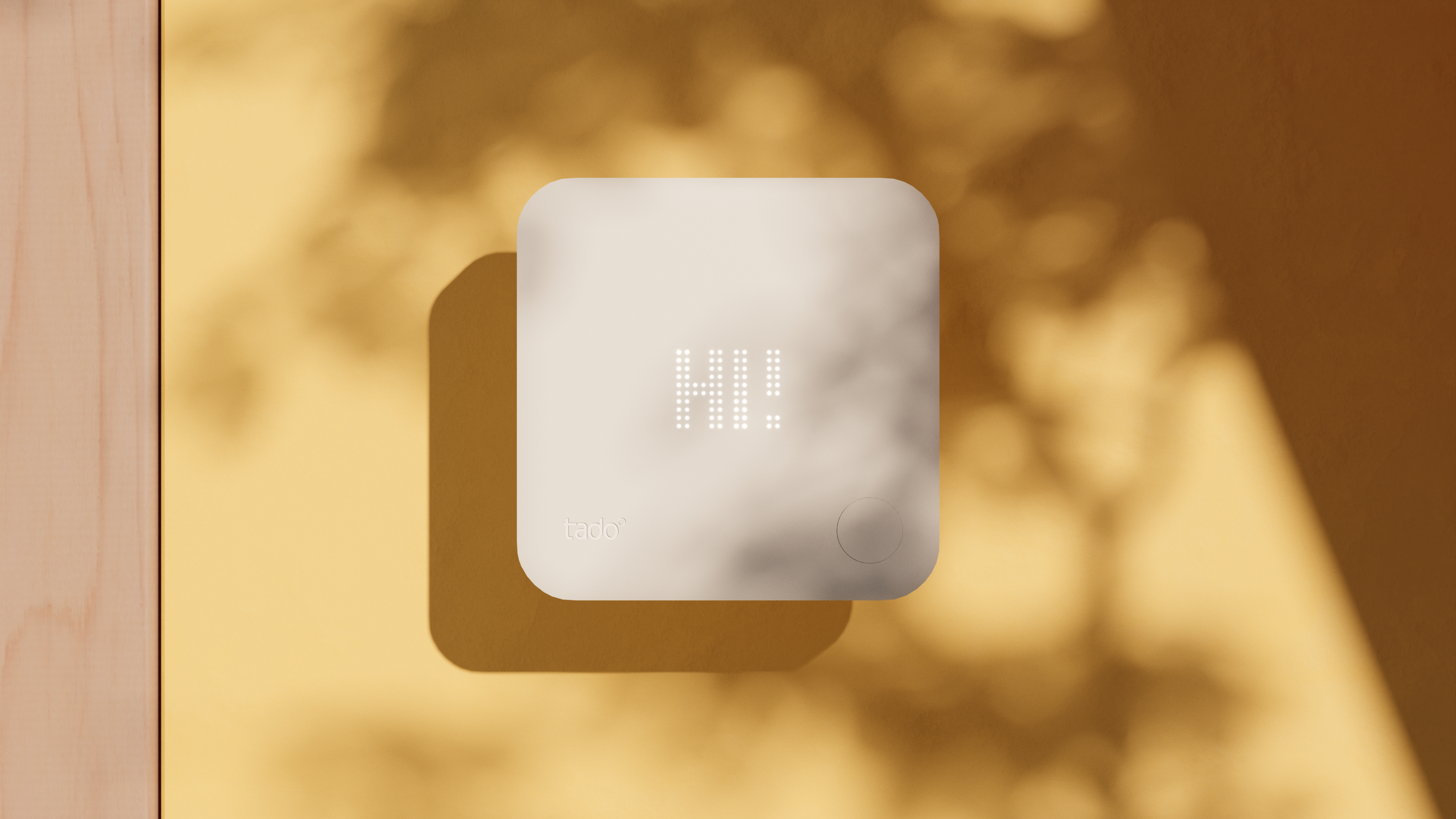 The tado smart thermostat floating in front of a yellow wall