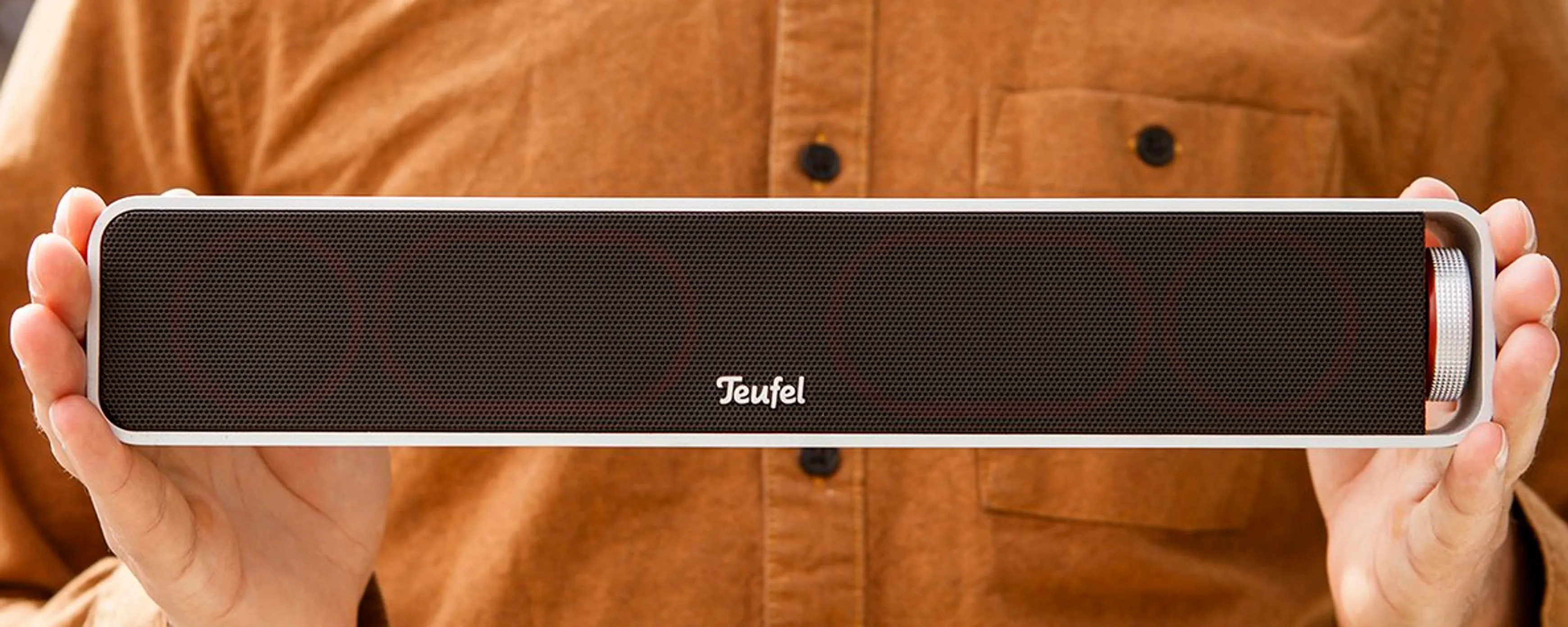 A person holding a Teufel Bamster speaker in front of themself