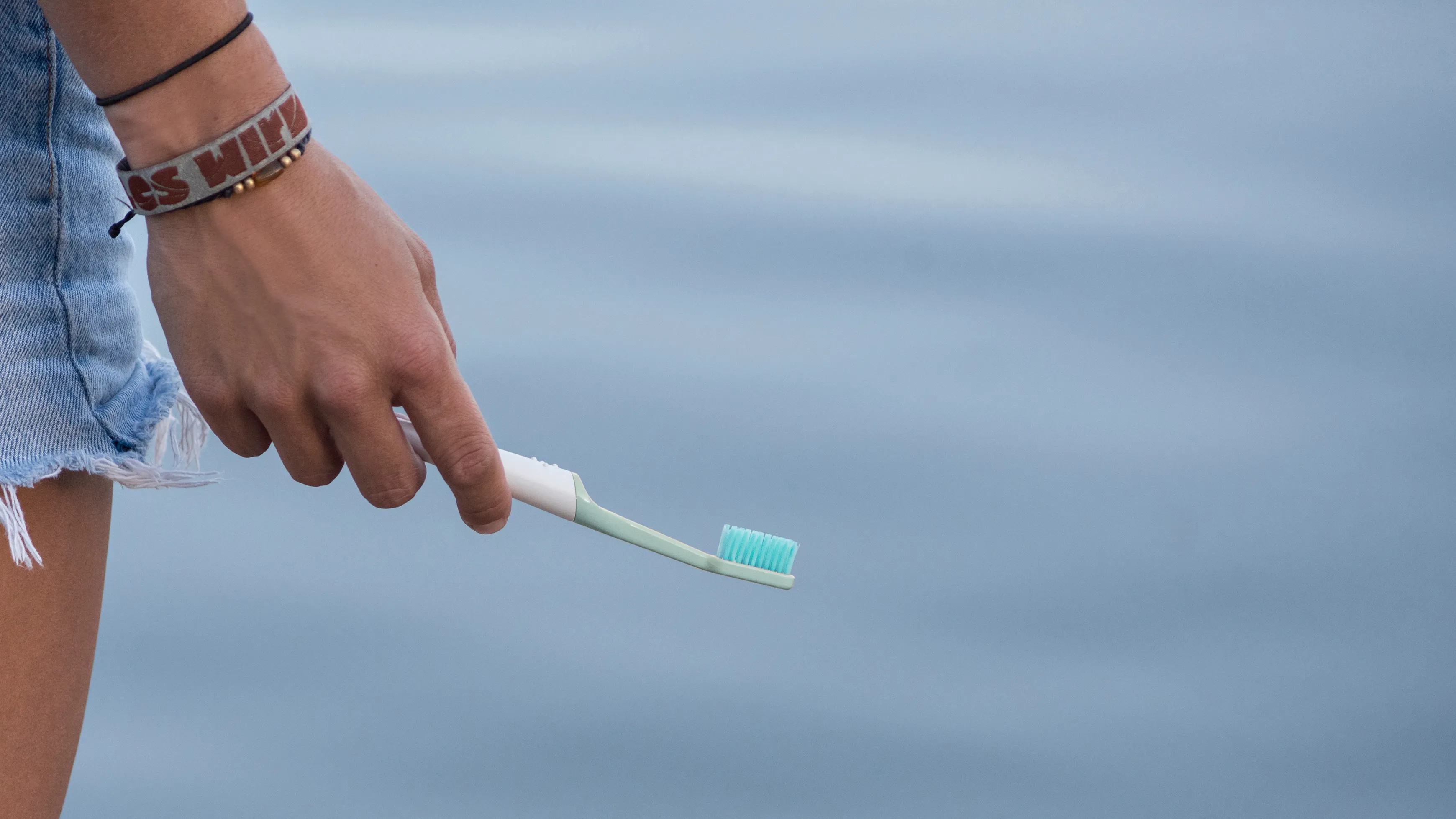 A hand holding a sustainable TIO toothbrush in front of the ocean