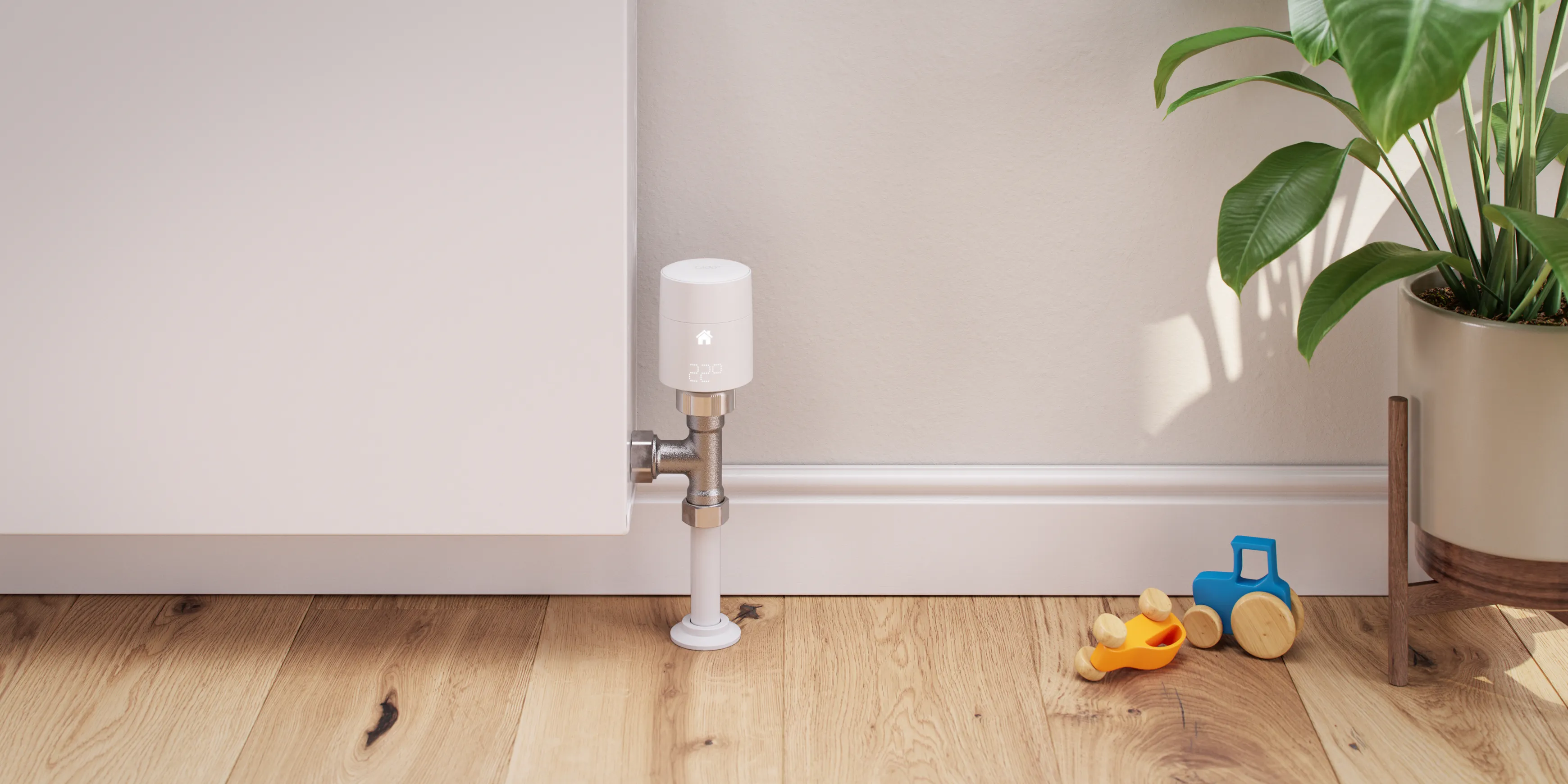 A tado smart heating radiator thermostat mounted on a radiator next to a potted plant and toys