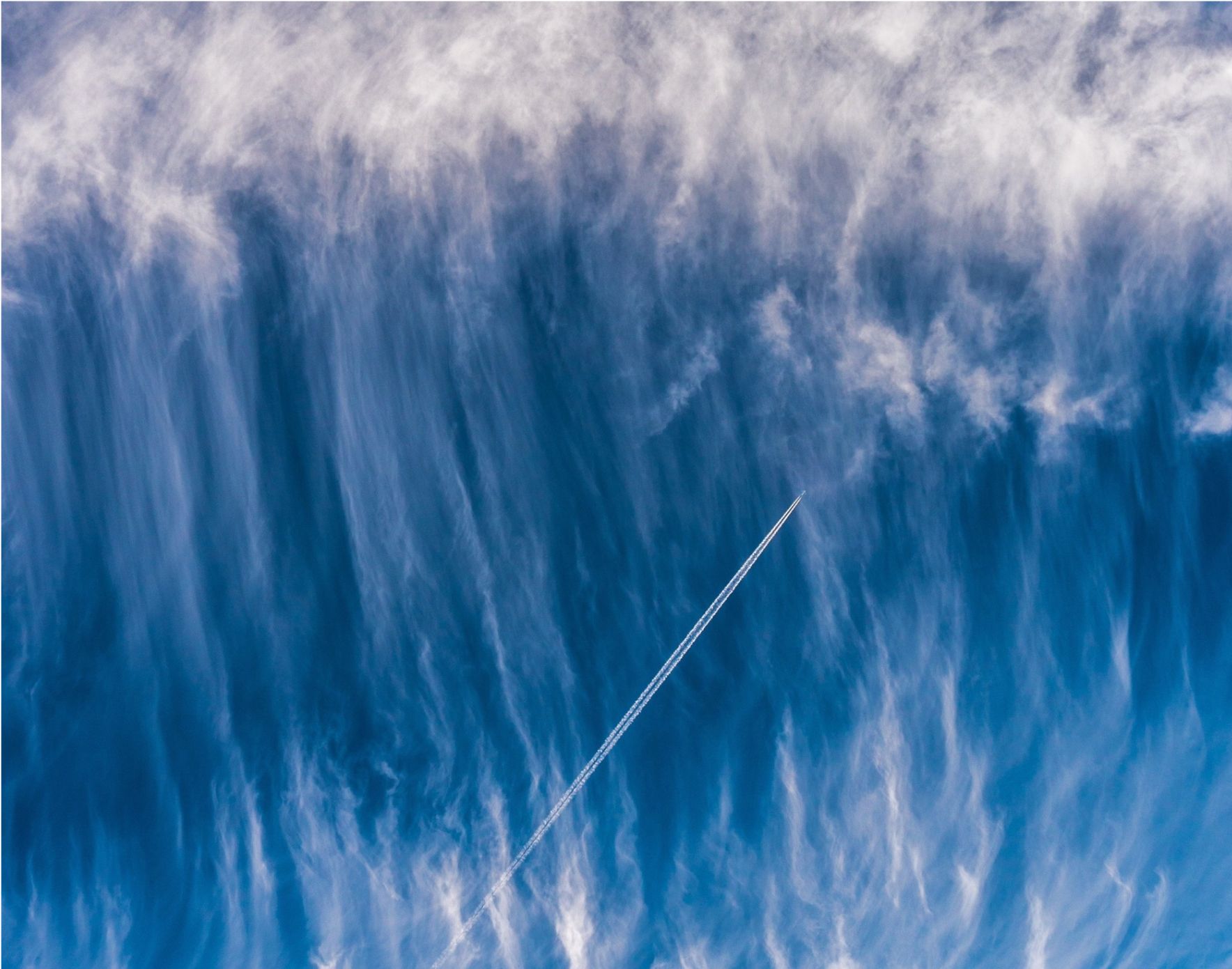 A plane's distinct contrail is visible as it flies into dramatic blue clouds