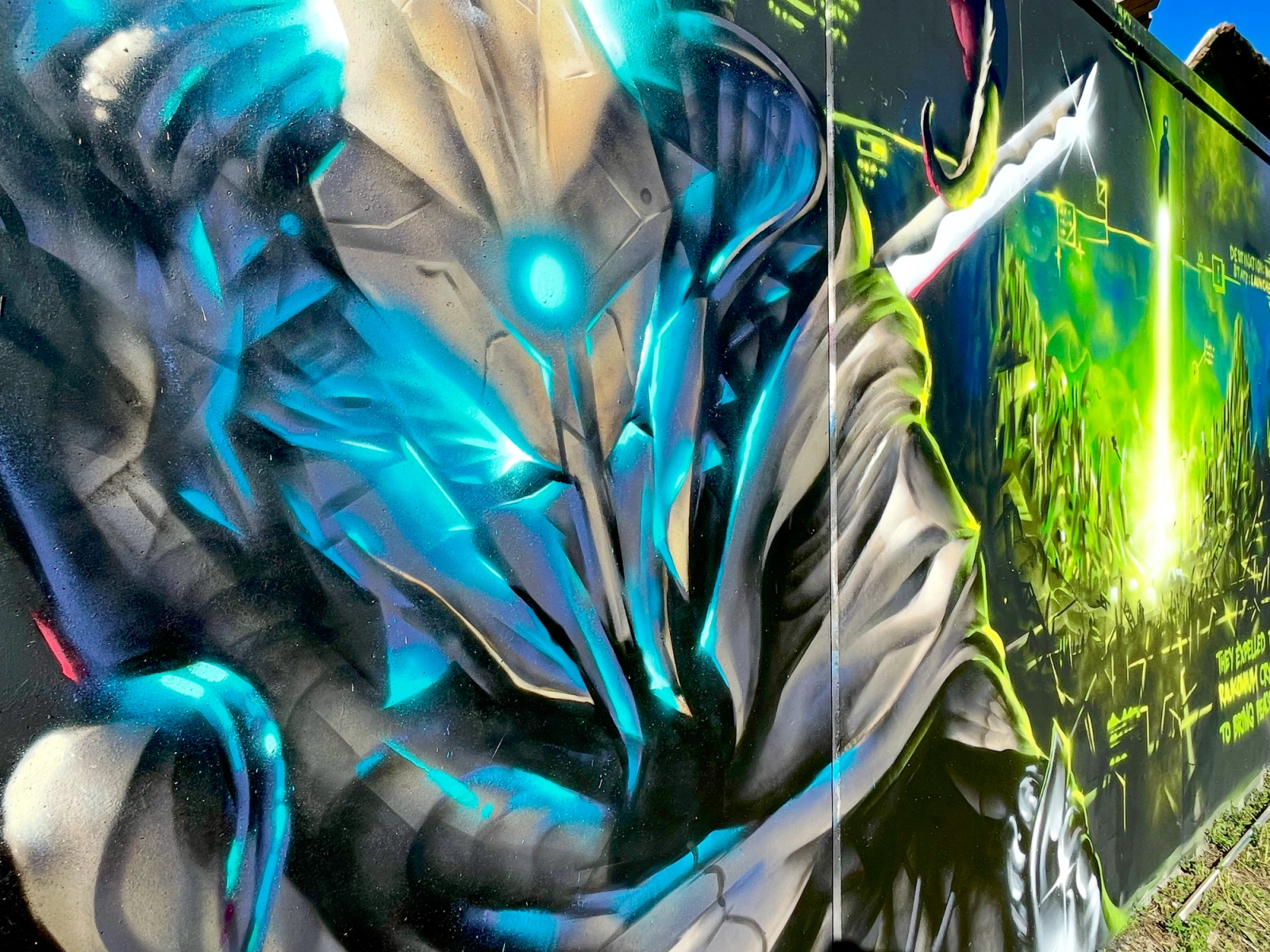 Närbild på rådets ledare i blå kromrustning bredvid en grön kristallstråle, del av en offentlig väggmålning i Visby på Gotland. Close-up of the hooded alien council leader in blue chrome armour beside a green crystal launch beam, part of a public mural in Visby, Gotland.