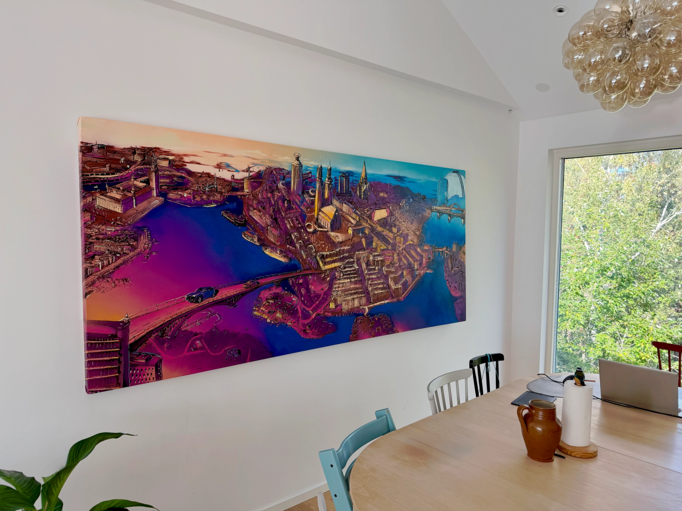 Den 250 x 110 cm stora Södermalmsmålningen ovanför ett matbord i ett ljust hem i Täby. The 250 x 110 cm Södermalm canvas hanging above a dining table in a bright home in Täby.