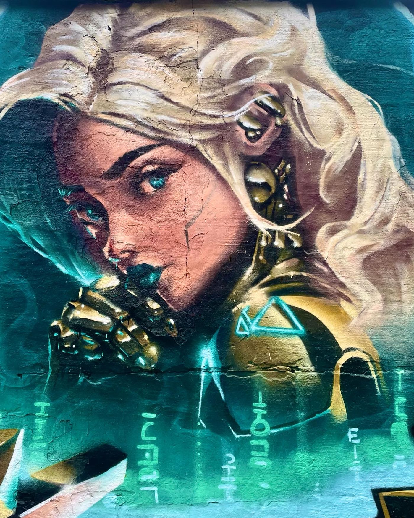 Spraymålad cyborgkvinna med blont hår, en gyllene mekanisk hand och grön binärkod, ur Age of AI-målningen i Snösätra. Spray-painted cyborg woman with blonde hair, a golden mechanical hand and green binary code, from the Age of AI mural in Snösätra.