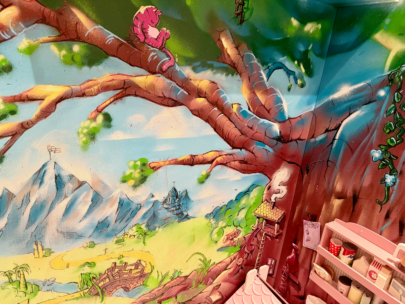 Detalj ur barnrumsmålningen med ett stort träd, blå berg och en solig äng. Detail of the magic forest kids' room mural with a large tree, blue mountains and a sunny meadow.