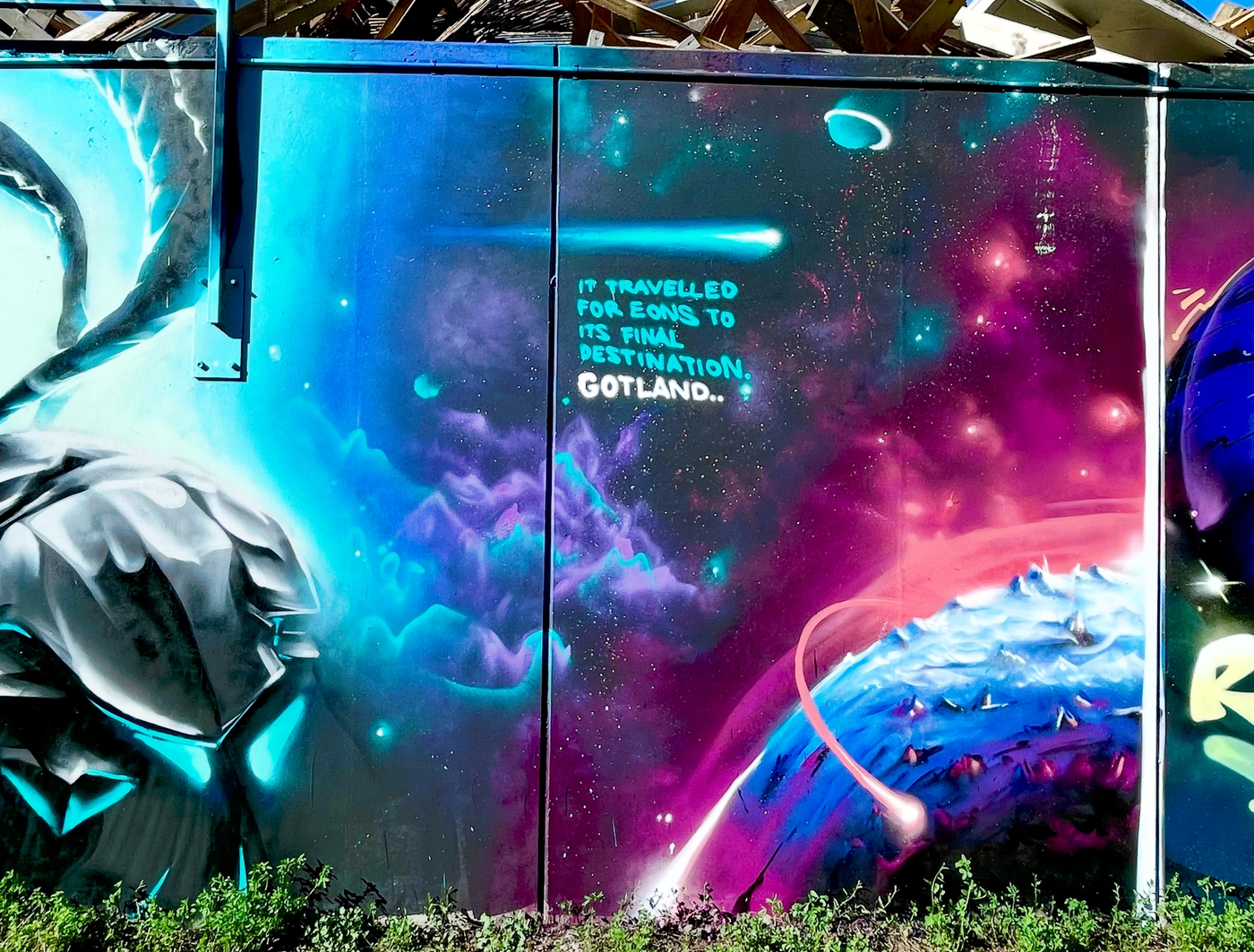 Rymdscen med jorden och en färdande kristall, målad på ett byggplank i Visby på Gotland. Space scene with planet Earth and a travelling crystal painted on a construction hoarding in Visby, Gotland.