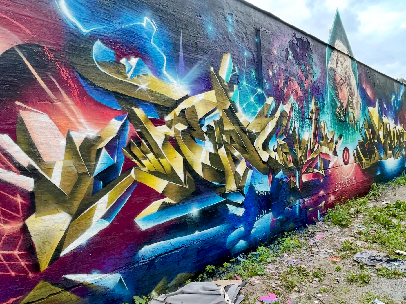 Guldiga 3D-graffitibokstäver med blixtar och en cyborgkvinna, Age of AI-väggen på Springbeast i Snösätra. Gold 3D graffiti letters with lightning and a cyborg woman, the Age of AI wall at Springbeast in Snösätra.