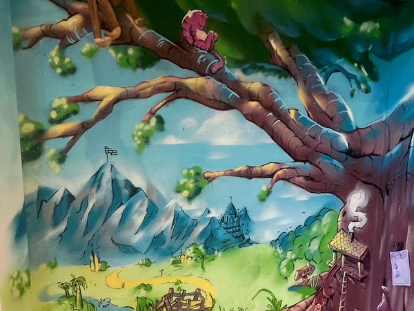Hörn i ett barnrum i Stockholm målat som en magisk skog med ett stort träd, berg och en äng, inspirerat av Nalle Puh. Kids' room corner in Stockholm painted as a magic forest with a big tree, mountains and a meadow, inspired by Winnie-the-Pooh.