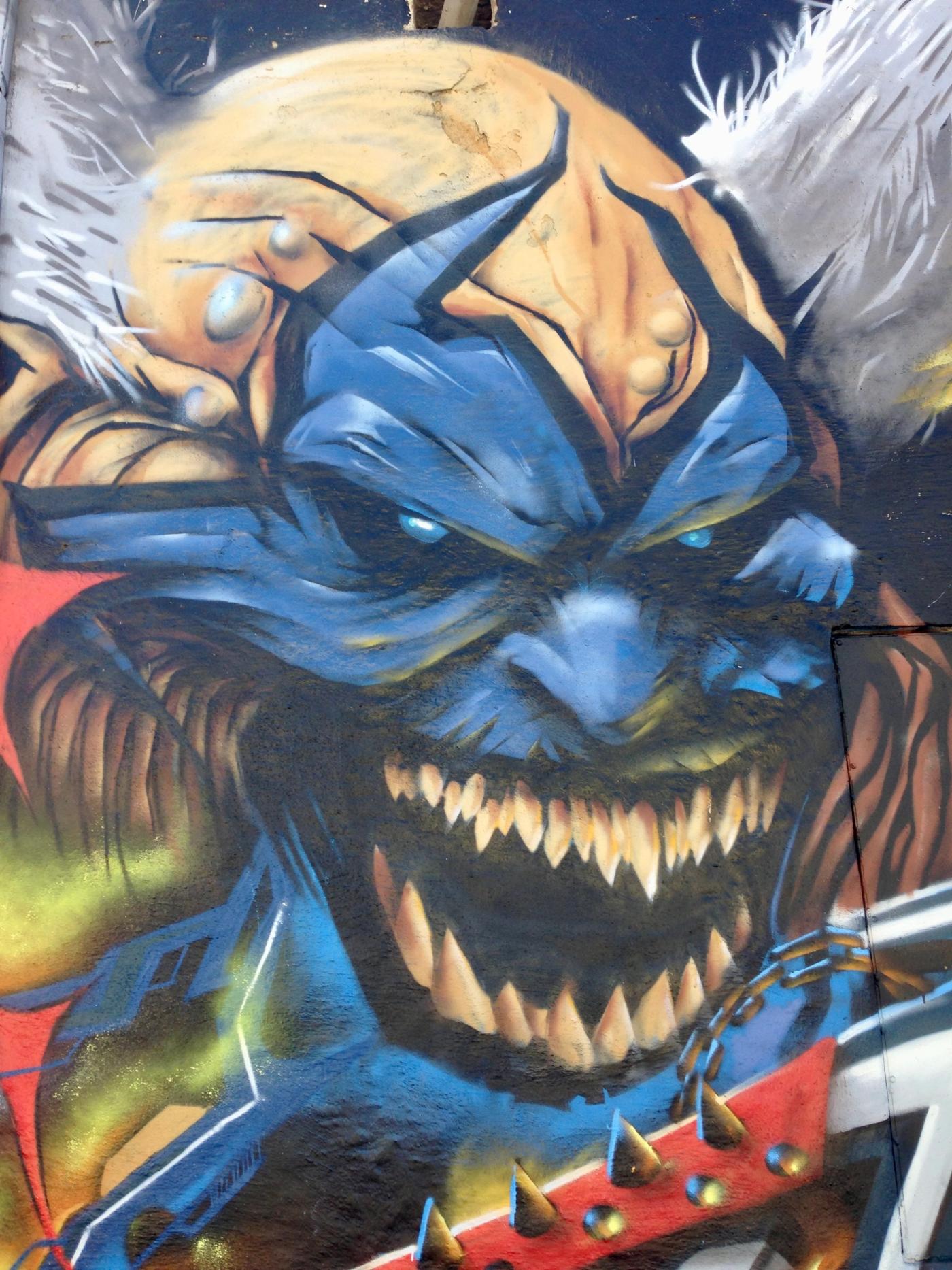 Närbild på Violators flinande blå ansikte på Spawn-väggen. Close-up of the grinning blue Violator face on the Spawn tribute wall.