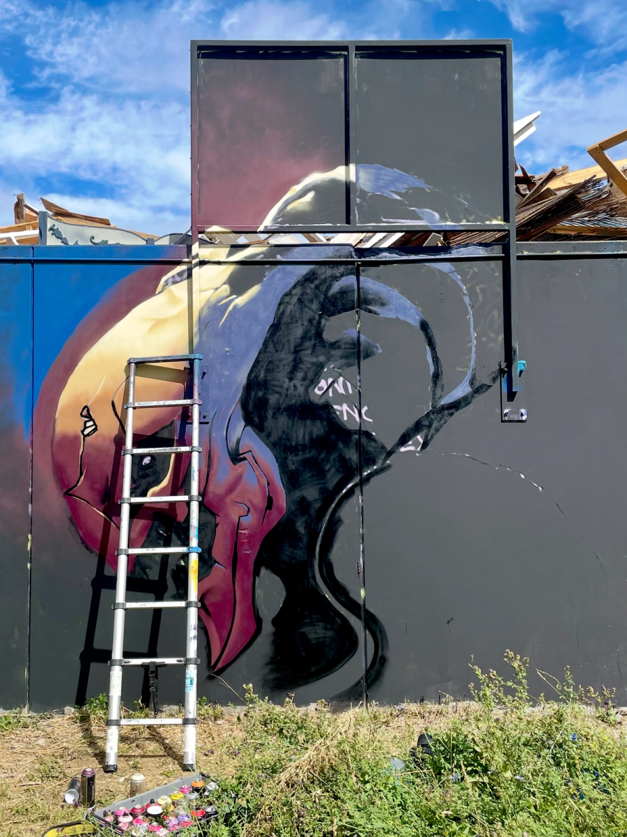 Tidigt skede av varelsemålningen i Visby med grundfärger, konturer och en stege mot väggen. Early stage of the alien creature mural in Visby, with base colours and outlines sprayed and a ladder against the wall.
