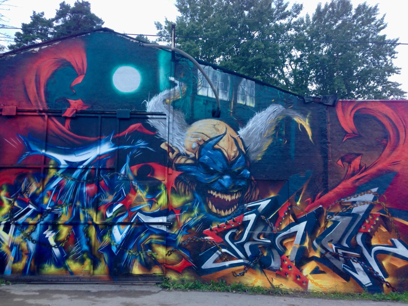 Violators demonansikte med graffitibokstäver, eld och kedjor, en Spawn-hyllning i Snösätra. Violator demon face with graffiti letters, flames and chains, a Spawn tribute mural in Snösätra.