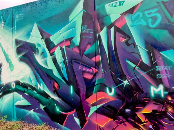 Turkosa och lila kristallbokstäver i graffiti på en lång vägg i Visby, kapitel 4 av The Raukonium Saga av Spraya. Teal and purple crystal graffiti letters on a long wall in Visby, chapter 4 of The Raukonium Saga by Spraya.