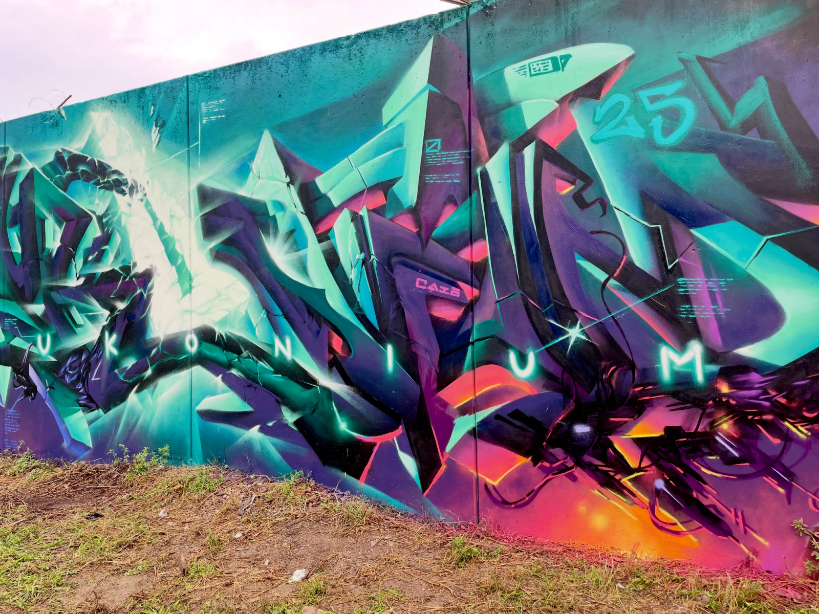 Turkosa och lila kristallbokstäver i graffiti på en lång vägg i Visby, kapitel 4 av The Raukonium Saga av Spraya. Teal and purple crystal graffiti letters on a long wall in Visby, chapter 4 of The Raukonium Saga by Spraya.