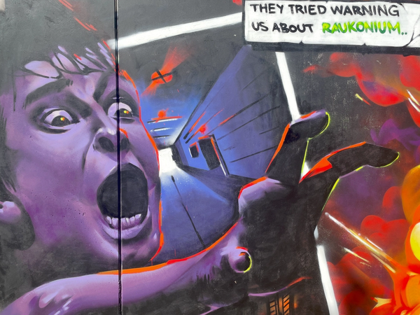 Graffitimålning i Visby av Spraya med en skrikande pojke, explosioner och en pratbubbla med texten They tried warning us about Raukonium. Graffiti mural in Visby by Spraya showing a screaming boy, explosions and a speech bubble reading They tried warning us about Raukonium.