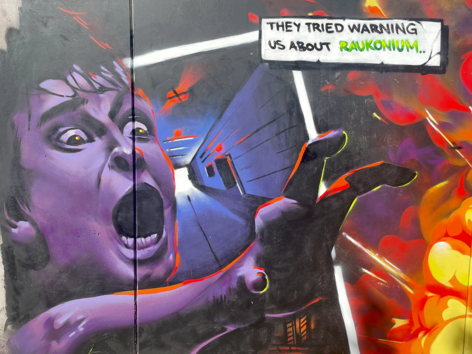 Graffitimålning i Visby av Spraya med en skrikande pojke, explosioner och en pratbubbla med texten They tried warning us about Raukonium. Graffiti mural in Visby by Spraya showing a screaming boy, explosions and a speech bubble reading They tried warning us about Raukonium.