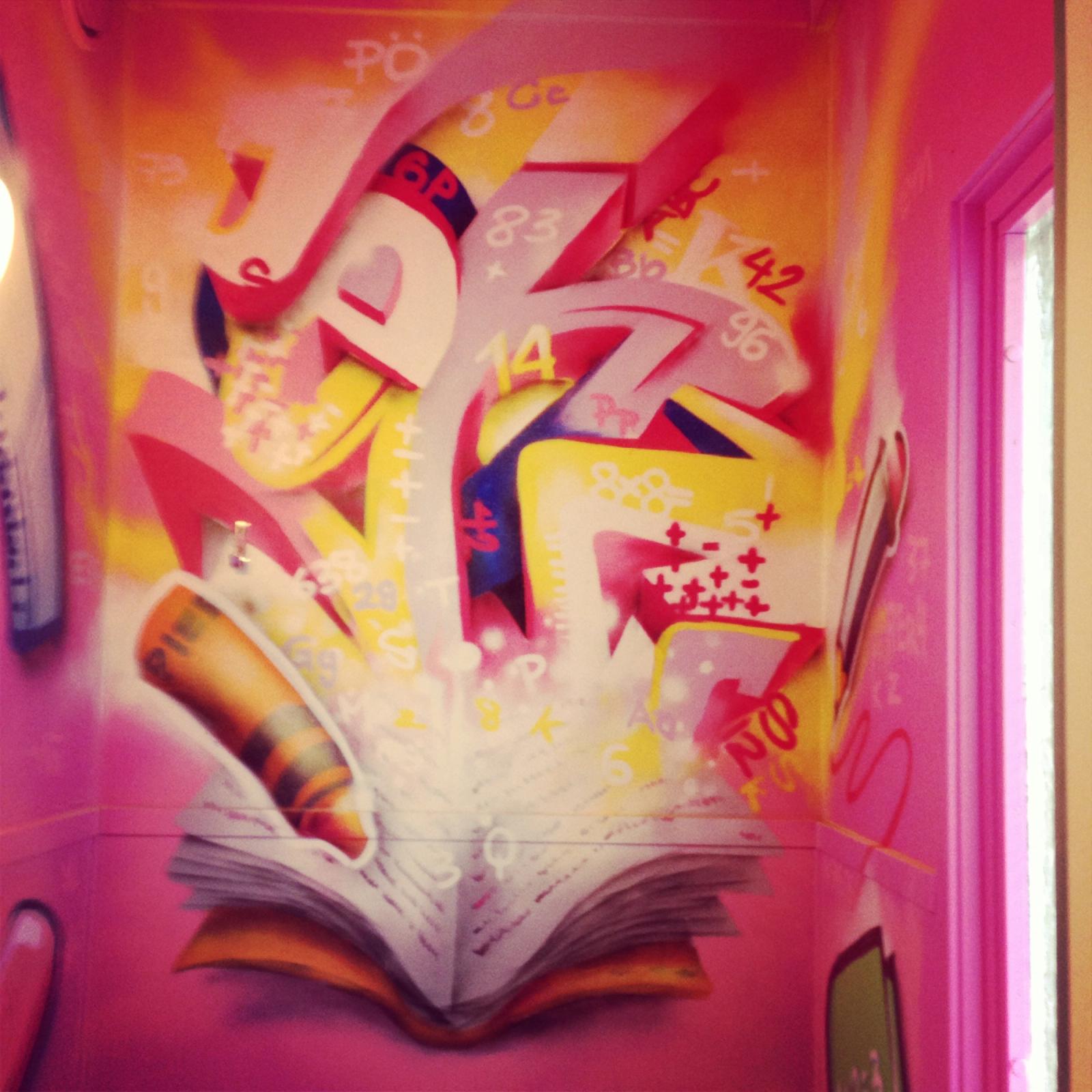 Hörn i en rosa skolkorridor där graffitibokstäver väller ut ur en uppslagen bok, väggmålning på Vibyskolan i Sollentuna. Corner of a pink school corridor with graffiti letters bursting out of an open book, a mural at Vibyskolan in Sollentuna.