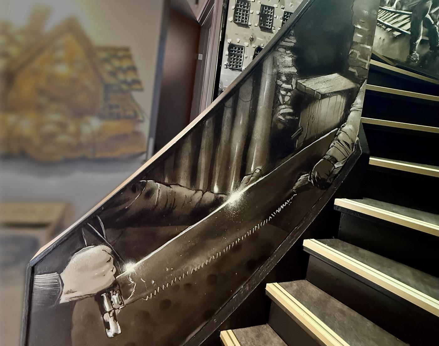 Trappa med en sepiafärgad Stockholmsmålning längs väggarna och den gyllene Lebe-maskoten synlig nedanför. Staircase with a sepia Stockholm mural running along the walls and the golden Lebe mascot visible below.