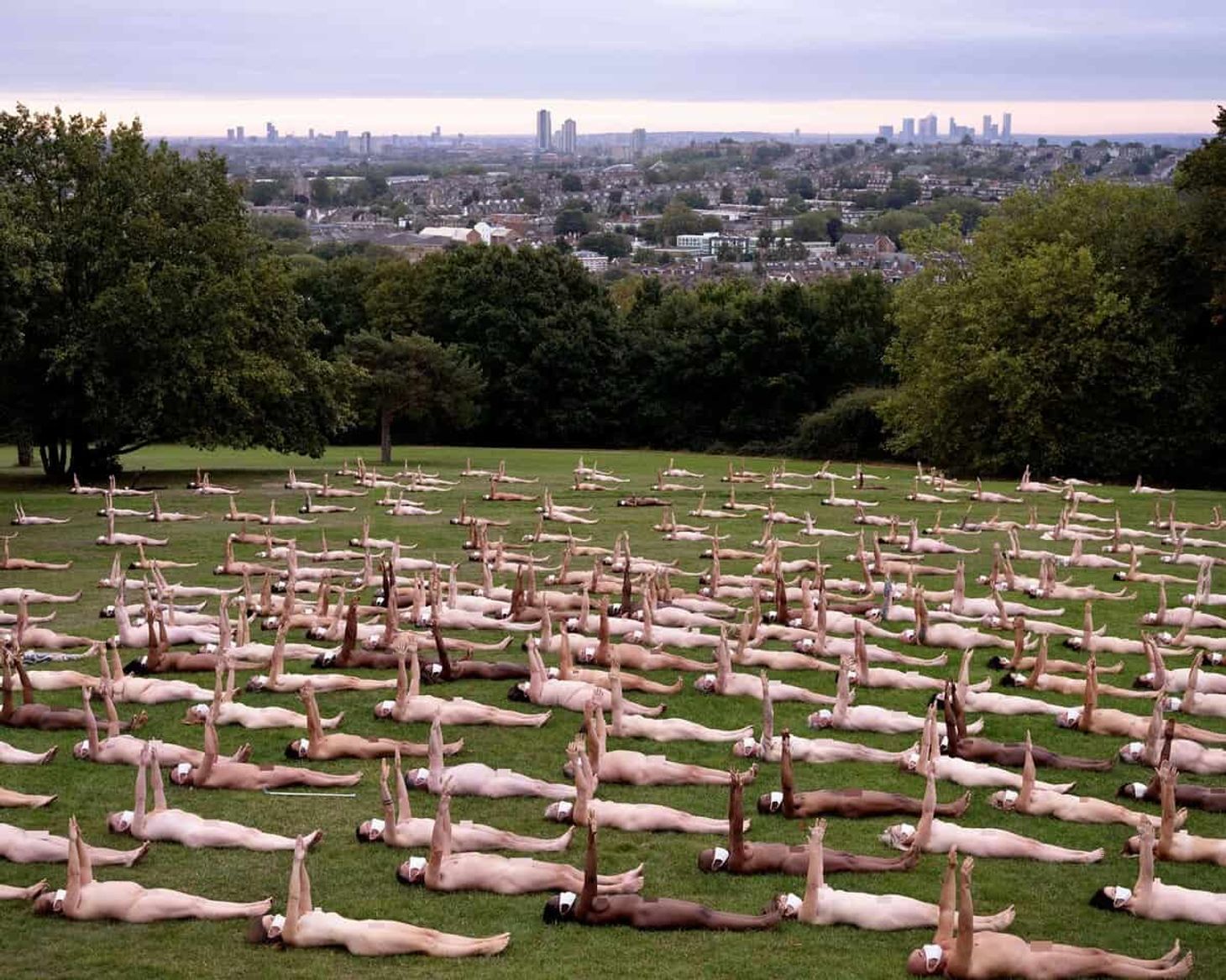 A group of naked people wearing covid face coverings laying on a large green with their arms in the air as part of a Sky Arts campaign