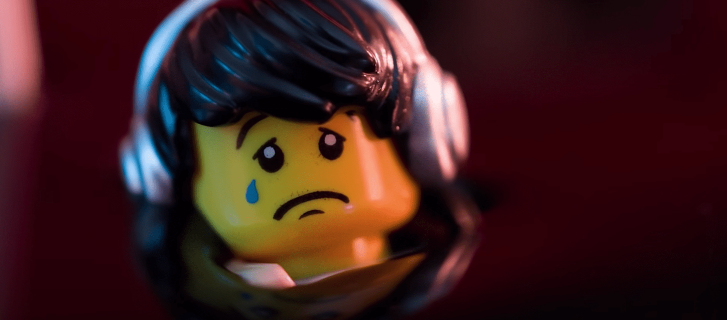 A lego figure with black hair and silver headphones with a sad expression and crying