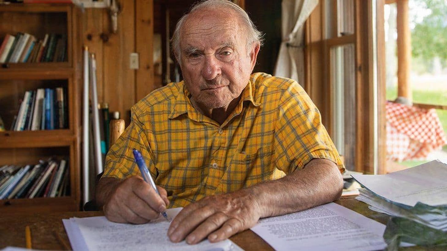 Yvon Chouinard, founder of the brand Patagonia wearing a yellow check shirt signing documents